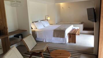 A bedroom with a bed, bedside tables, a wooden bench, a TV, and a bathroom with a bathtub and shower.