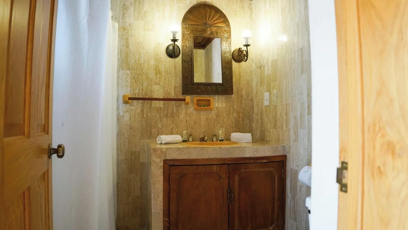 A bathroom with a wooden vanity, a mirror with a decorative frame, and wall-mounted lighting.