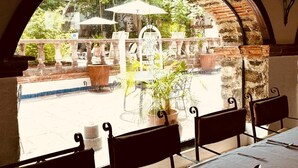 A restaurant with outdoor seating, a stone archway, and a view of a pool and greenery. - Hotel Ex-Hacienda La Pitaya Queretaro (Apaseo el Grande)