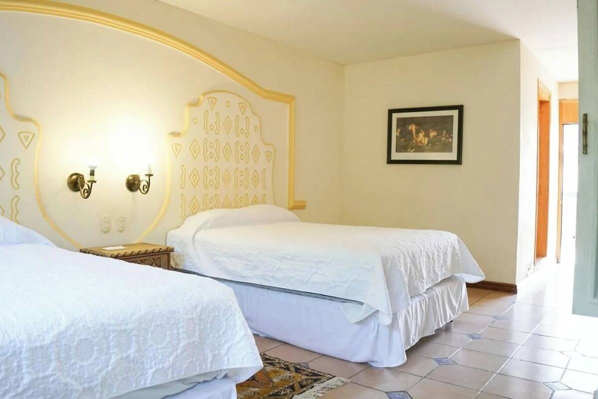 Ein Hotelzimmer mit zwei Betten, einer strukturierten Wand, einem gerahmten Bild und einem Fliesenboden.