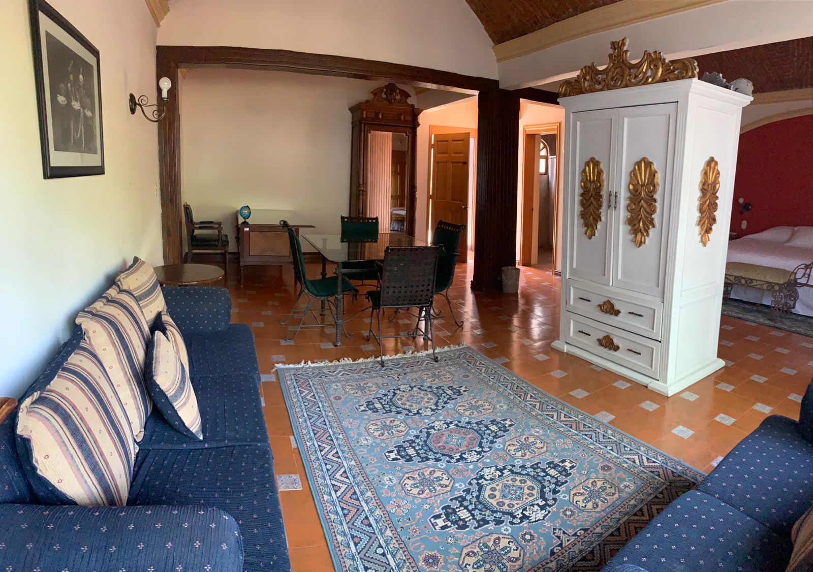 Une pièce comprenant un canapé, un tapis à motifs, un meuble et un coin repas avec des chaises et une table.