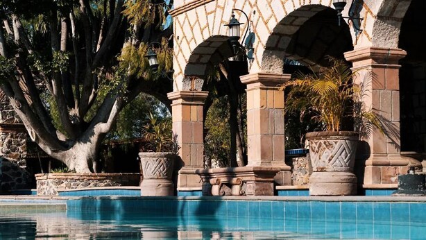 A pool area with stone columns and arches, surrounded by trees and potted plants. - Hotel Ex-Hacienda La Pitaya Queretaro (Apaseo el Grande)