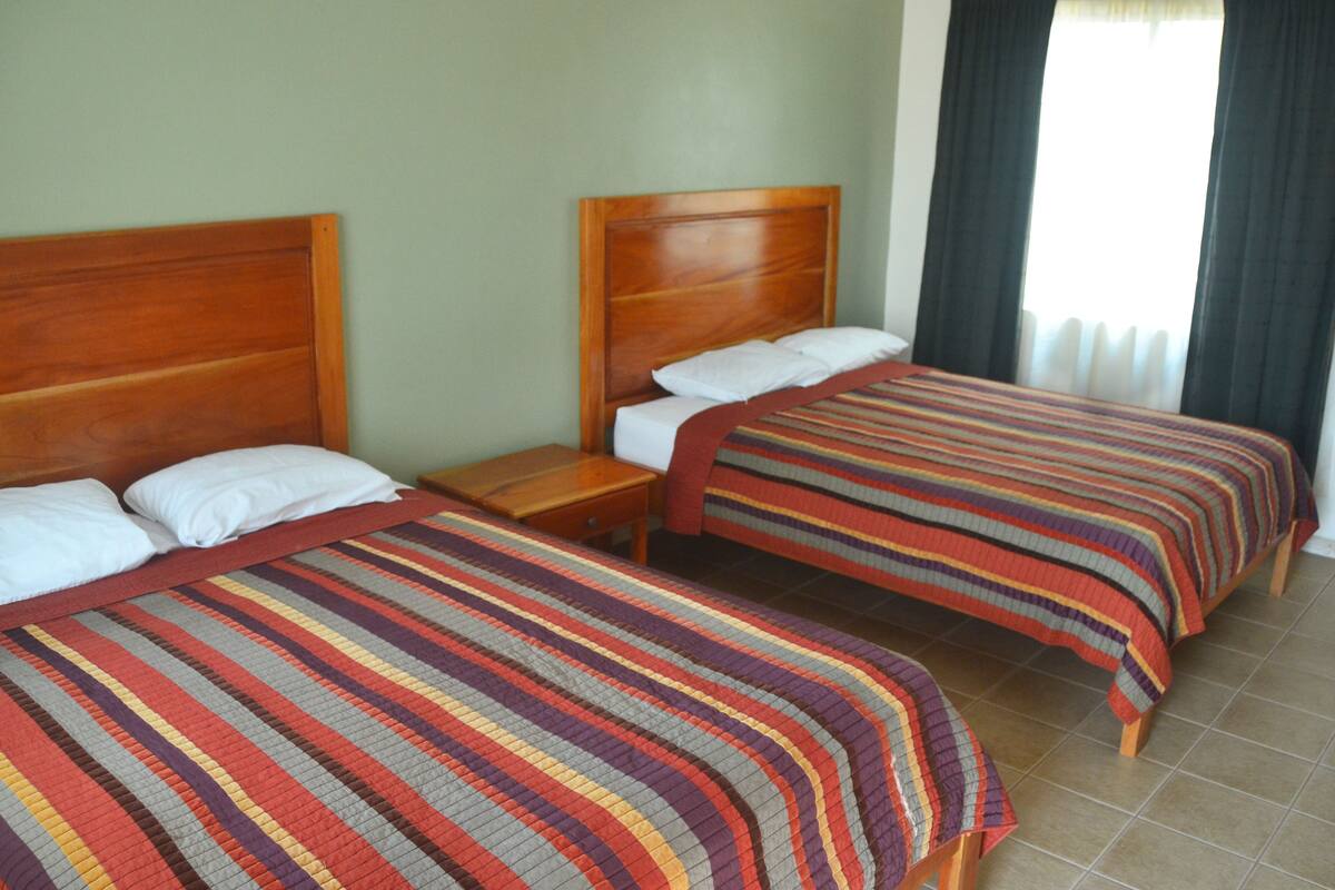 Two single beds with wooden headboards, a nightstand, and a striped bedspread.