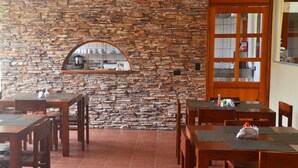 A restaurant with stone walls, wooden tables, and a kitchen visible through a window. - Hotel La Villa (Quesada)