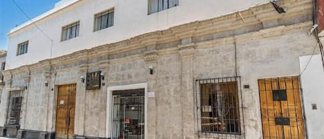 A two-story building with a white facade, multiple windows, and doors with metal bars.