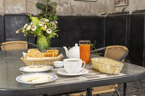 A breakfast table with bread, a teapot, a cup of coffee, a glass of orange juice, and a small bowl of cream.