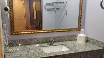 Um banheiro com bancada de granito, pia, espelho com moldura dourada, dispensador de toalhas e secador de cabelo.