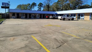 A motel with a blue roof and multiple rooms, a parking lot with several vehicles, and a sign indicating 100+ HD channels.