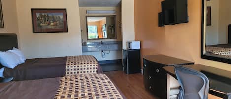 Een hotelkamer met twee bedden, een bureau, een stoel, een televisie, een spiegel en een badkamer zichtbaar door een geopende deur.