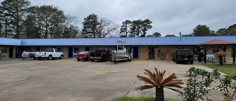 A building with a blue roof and brick walls, parking lot, and a covered area with tables and chairs.