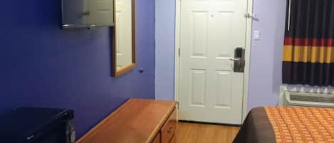 Ein Hotelzimmer mit einem Holzschrank, einem Bett mit gemustertem Überwurf, einer weißen Tür und einem Spiegel an der Wand.