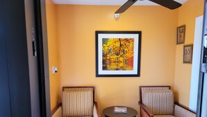 A hotel room with two patterned armchairs, a small round table with a magazine, and a framed picture of autumn leaves on the wall.
