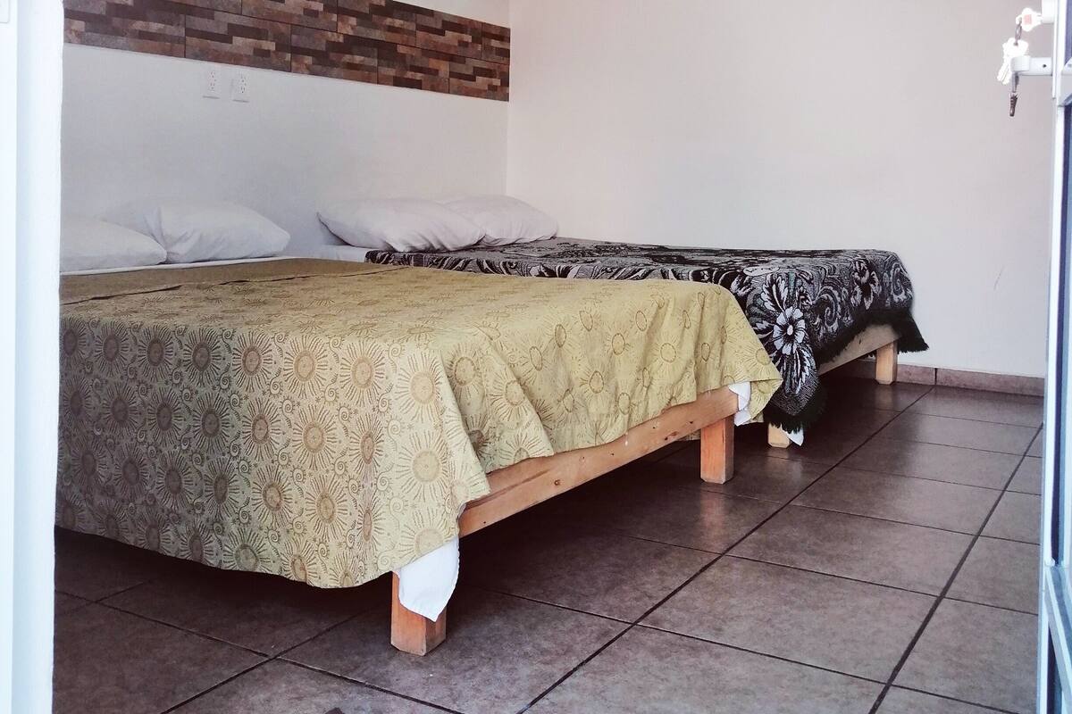 A room with two beds, a wall-mounted shelf, a door with a handle, and a welcome mat.