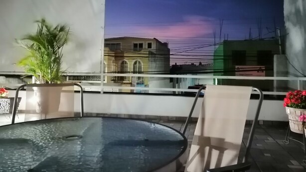 A balcony with a glass-top table, chairs, and potted plants. - Hostal Maple (Querétaro)