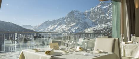 A dining area with tables set for a meal, overlooking a snowy mountain range.