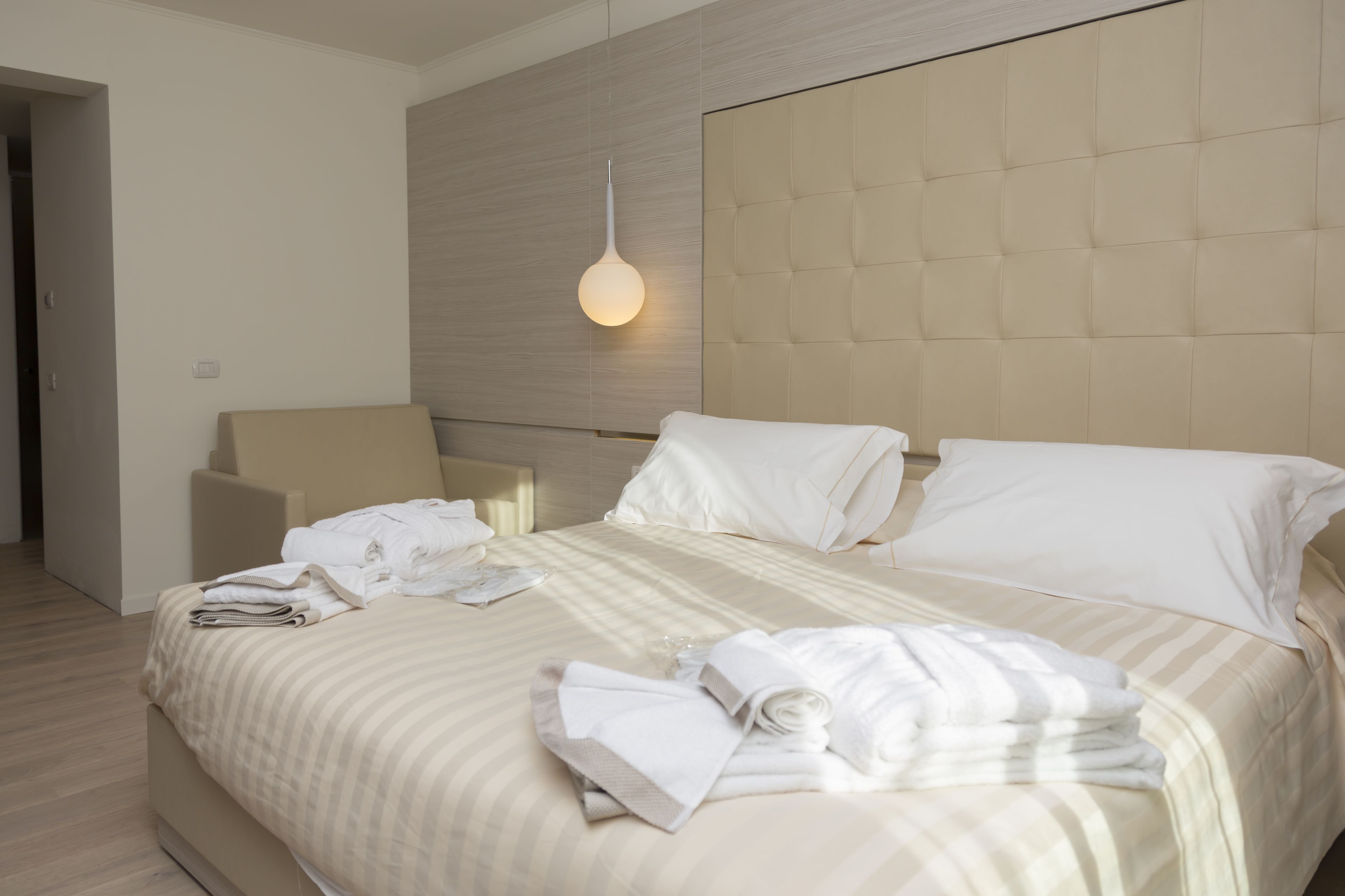 A modern hotel room with a large bed, a headboard, and a hanging light fixture.
