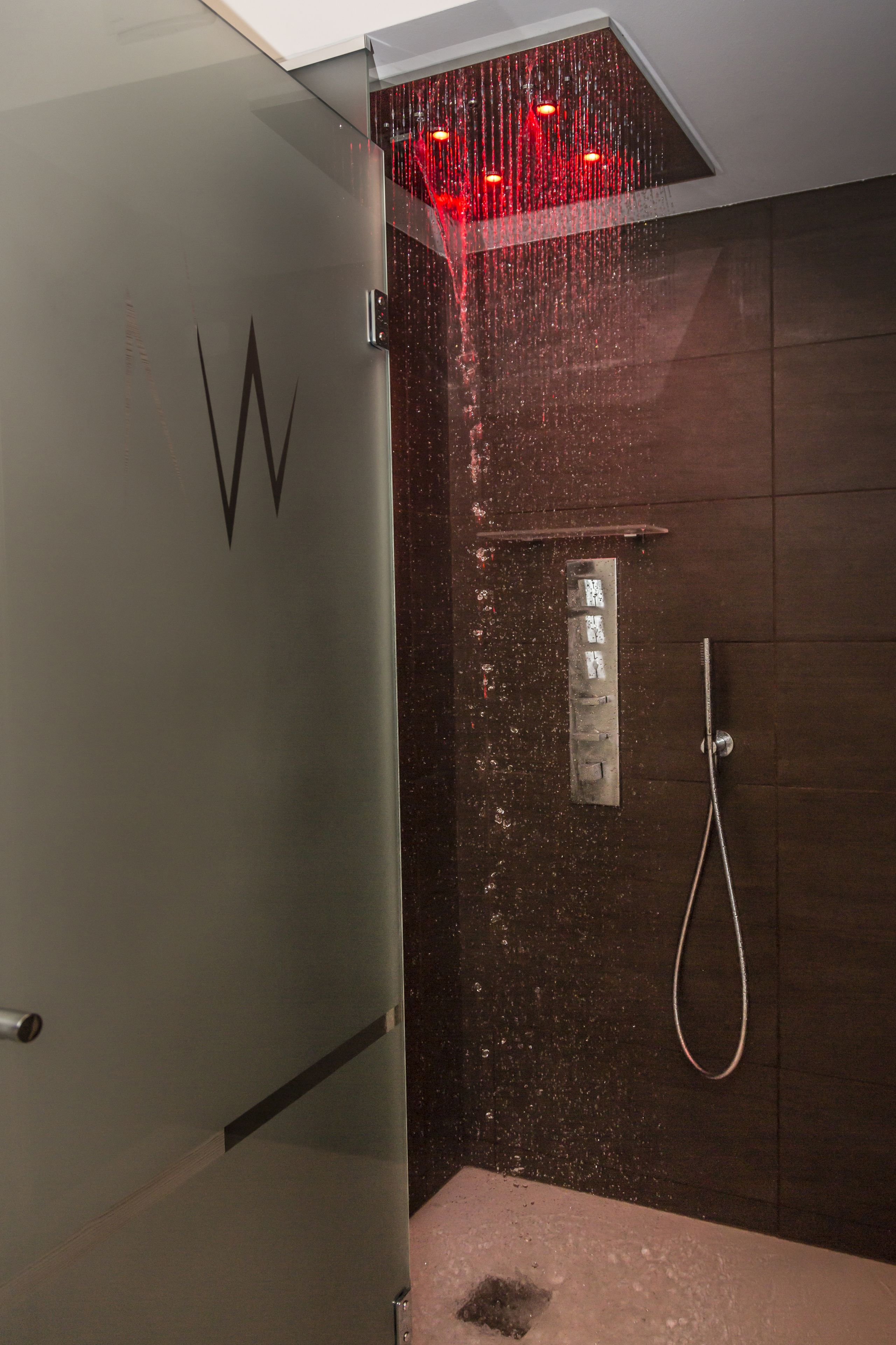A shower with a glass door, a metal handle, and a showerhead with red lights.