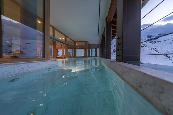An indoor swimming pool with clear glass walls, a view of a snowy mountain, and a modern architectural design. - White Angel Hotel (Valtournenche)
