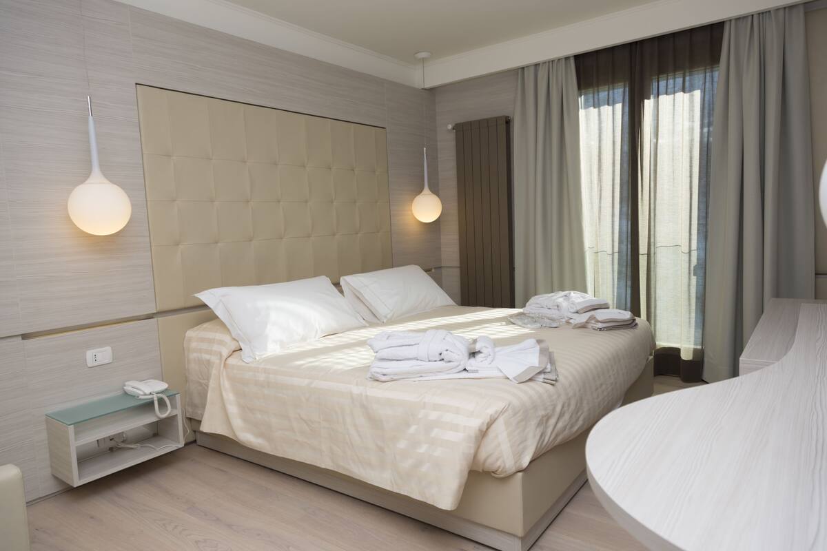 Habitación de hotel moderna con una cama grande, una mesita de noche con teléfono y un estante de vidrio.