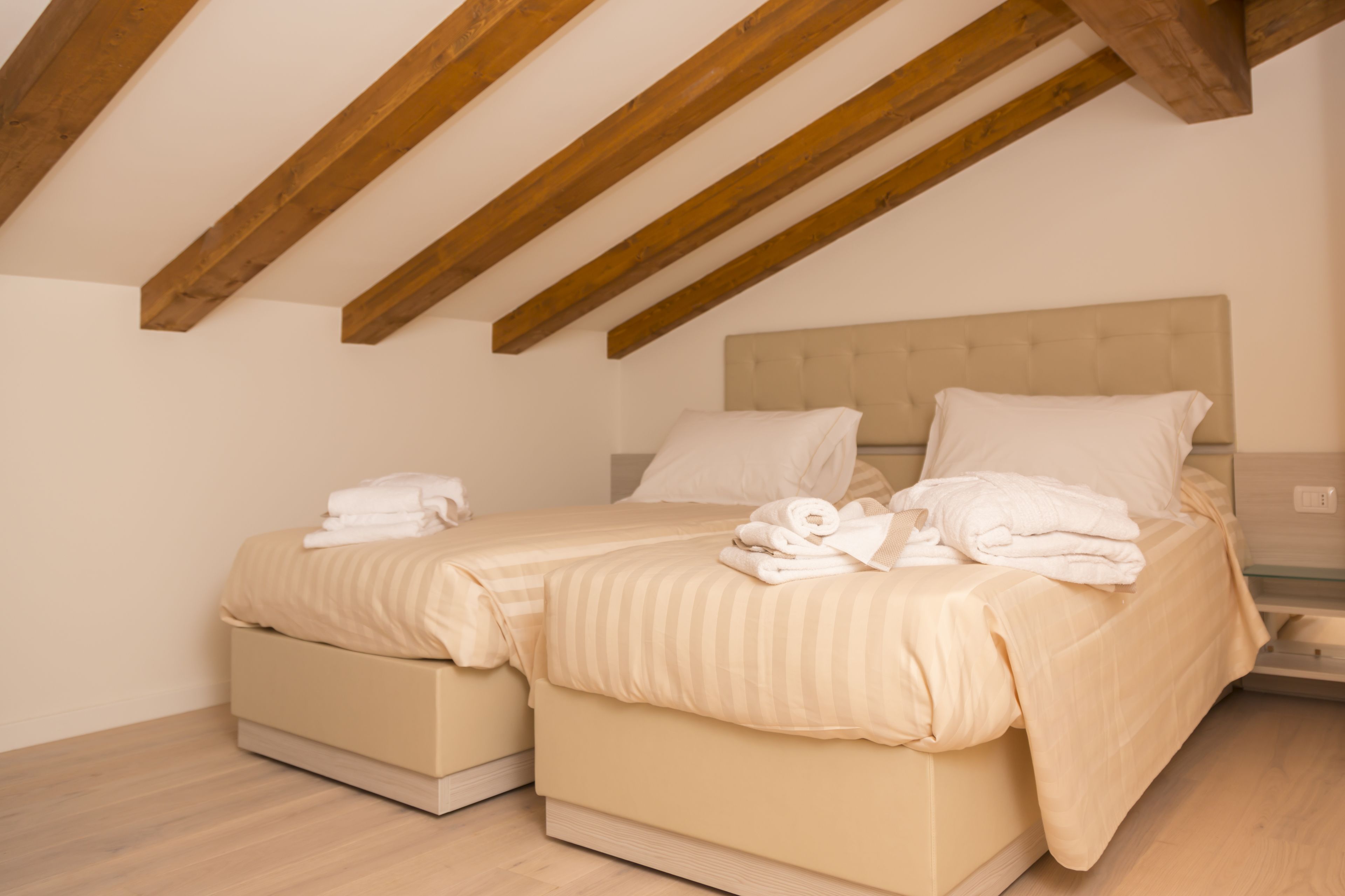 A bedroom with two beds, wooden beams on the ceiling, and a neutral color scheme.