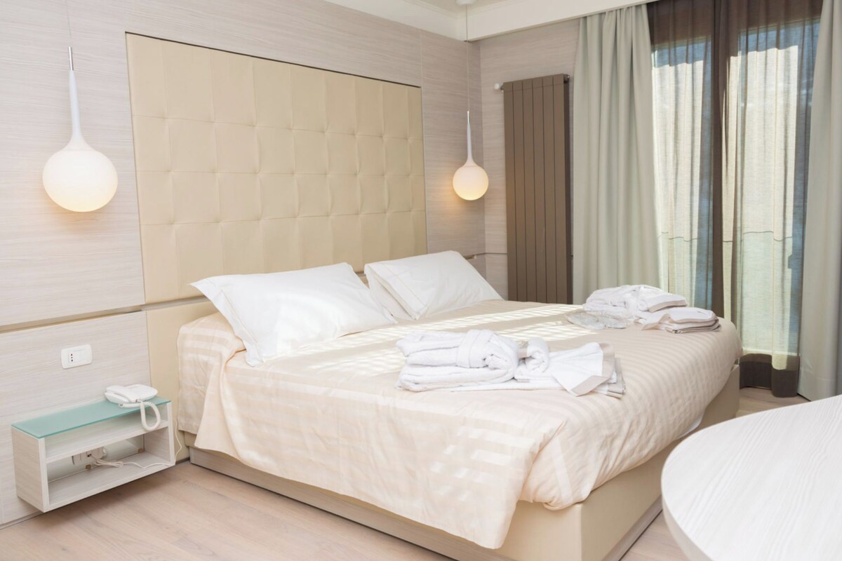 A modern hotel room with a large bed, a bedside table with a phone, and a window with curtains.