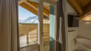 Una habitación con techo de madera, puerta de vidrio corredera que da a un balcón con vistas a la montaña y un televisor montado.