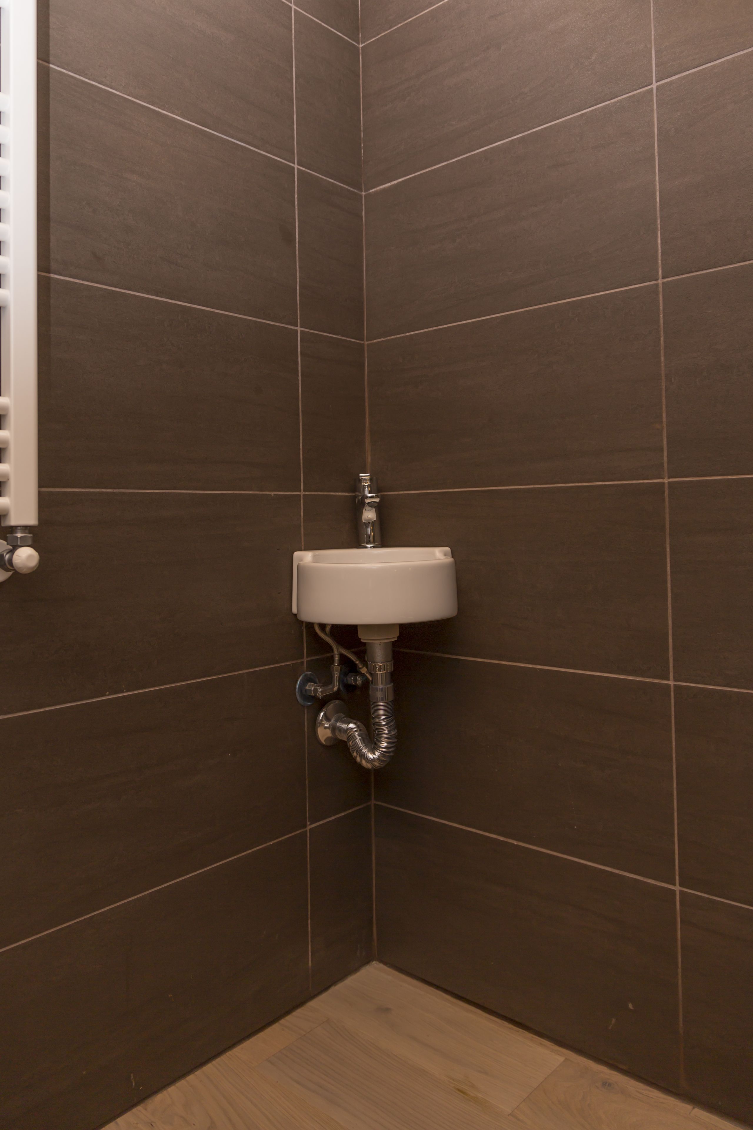 A bathroom with dark brown tiles, a white sink, and a visible pipe.