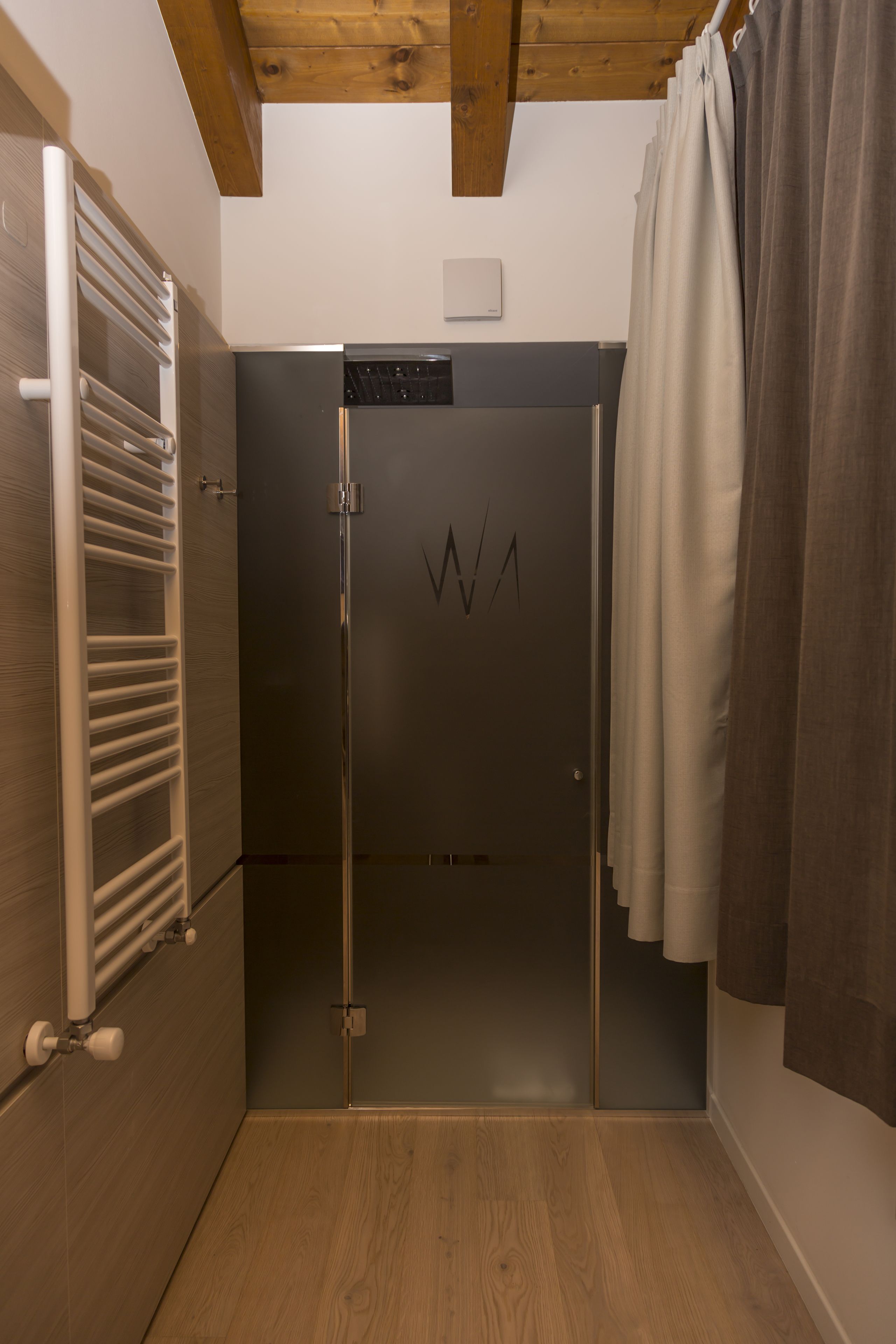 Une salle de bain moderne et compacte, dotée d’une douche, d’un porte-serviettes et d’une porte ornée d’un logo.