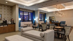 En hotelllobby med en sittgrupp, en receptionsdisk och utsikt över stadsbilden genom stora fönster.