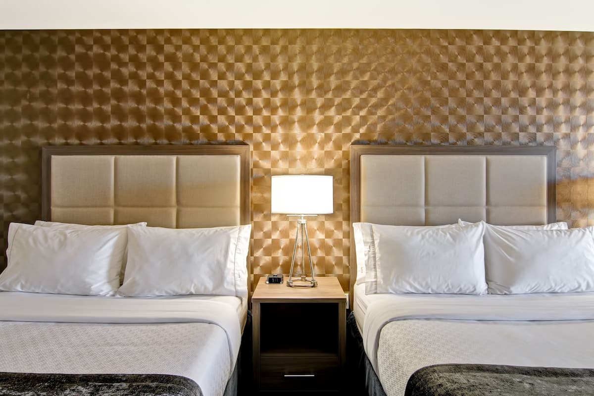 A hotel room with two beds, a checkered headboard, a bedside table with a lamp, and a clock.