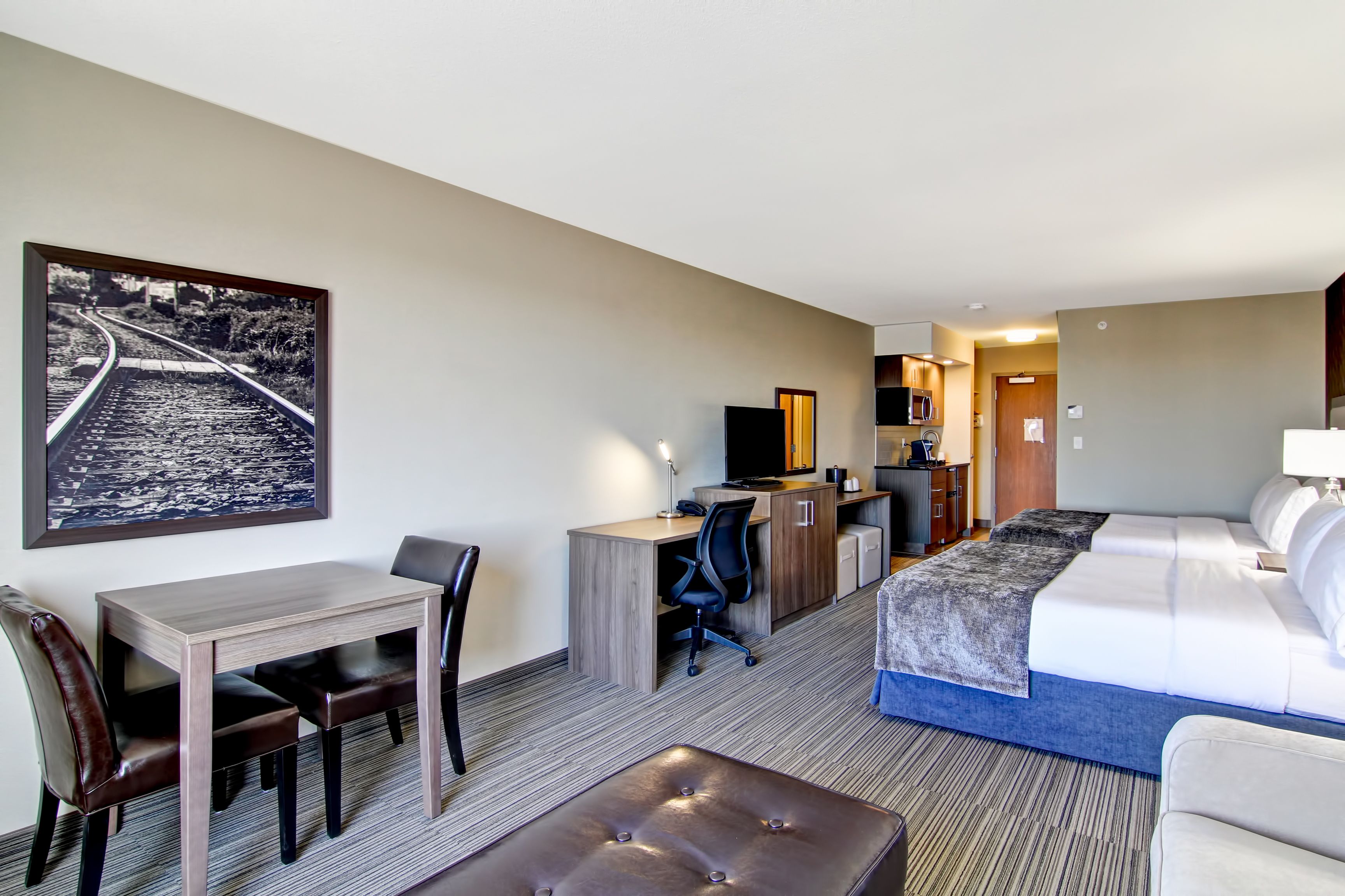 Habitación de hotel con cama, escritorio con silla, una mesita pequeña y un cuadro grande en la pared.