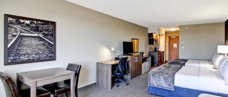 Habitación de hotel con cama, escritorio con silla, una mesita pequeña y un cuadro grande en la pared.