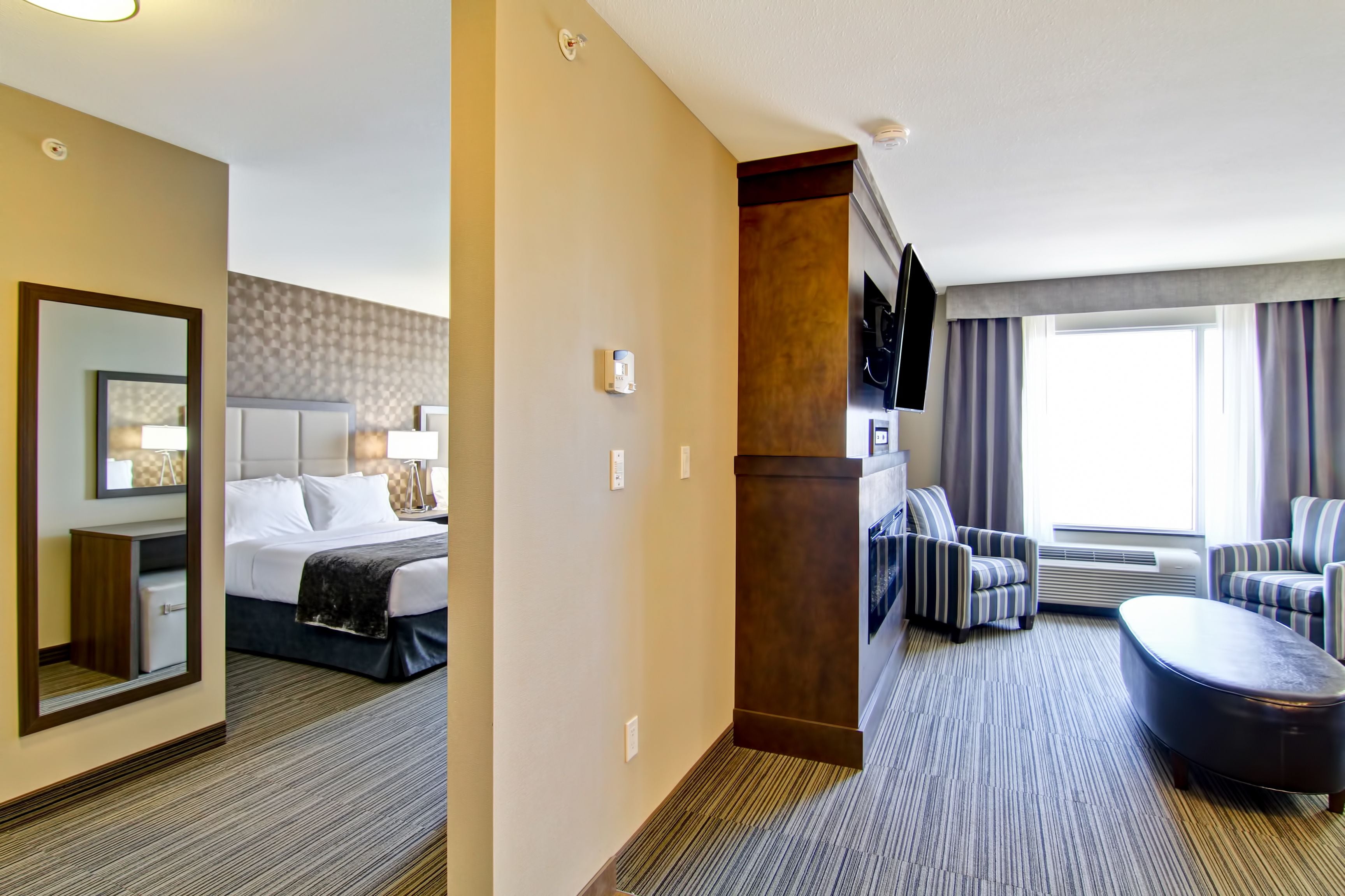 A hotel room with a bed, a desk, a chair, a sofa, and a large window.