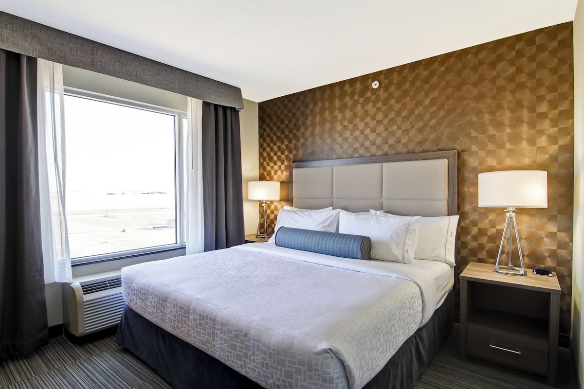 Habitación de hotel con una cama grande, dos mesitas de noche con lámparas, una ventana con cortinas y un papel tapiz estampado.