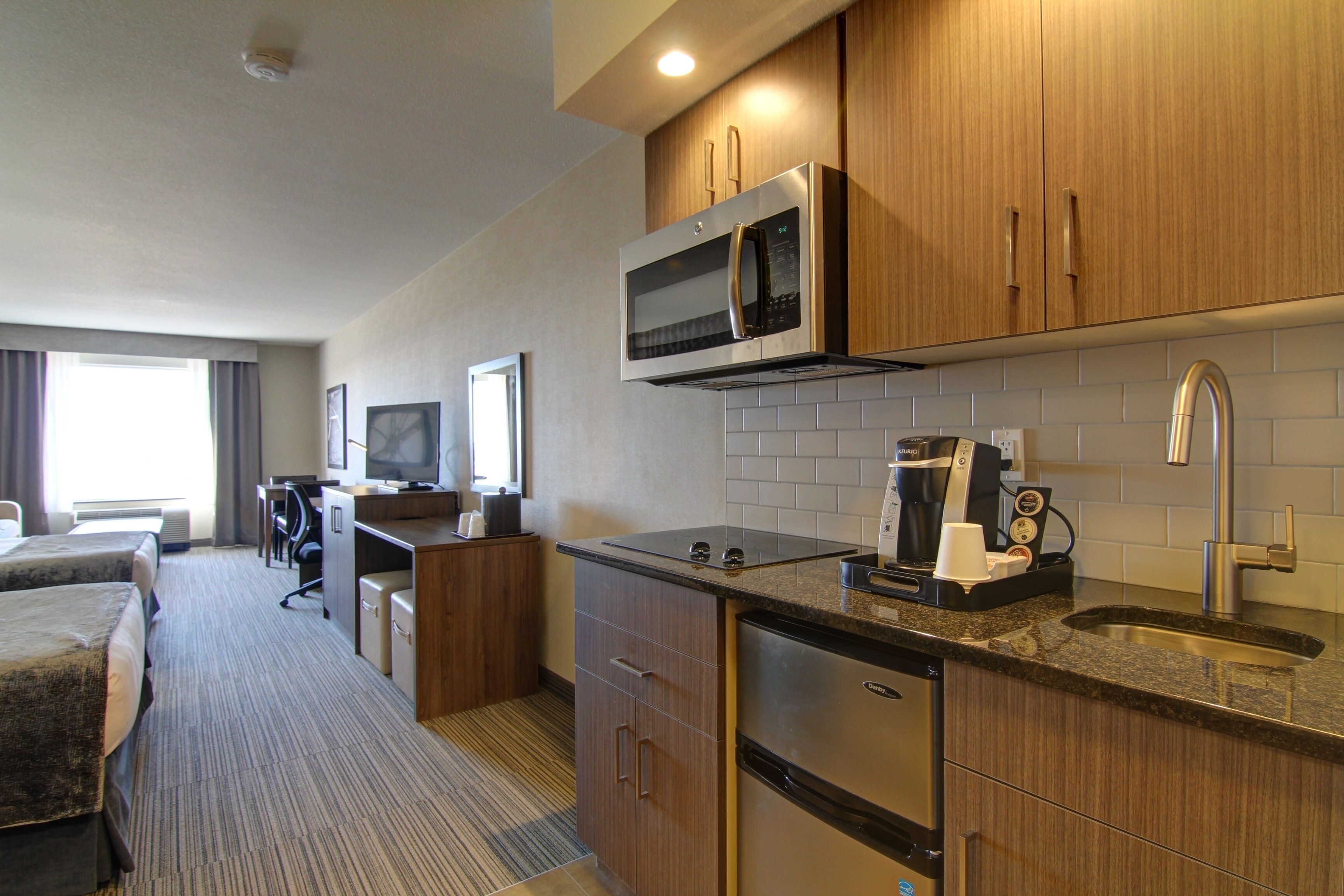 A hotel room with a kitchenette, a bed, a desk, and a television.
