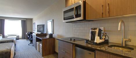 A hotel room with a kitchenette, a bed, a desk, and a television.