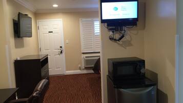 A hotel room with a flat-screen TV mounted on the wall, a refrigerator, a microwave, a door, and a patterned carpet.