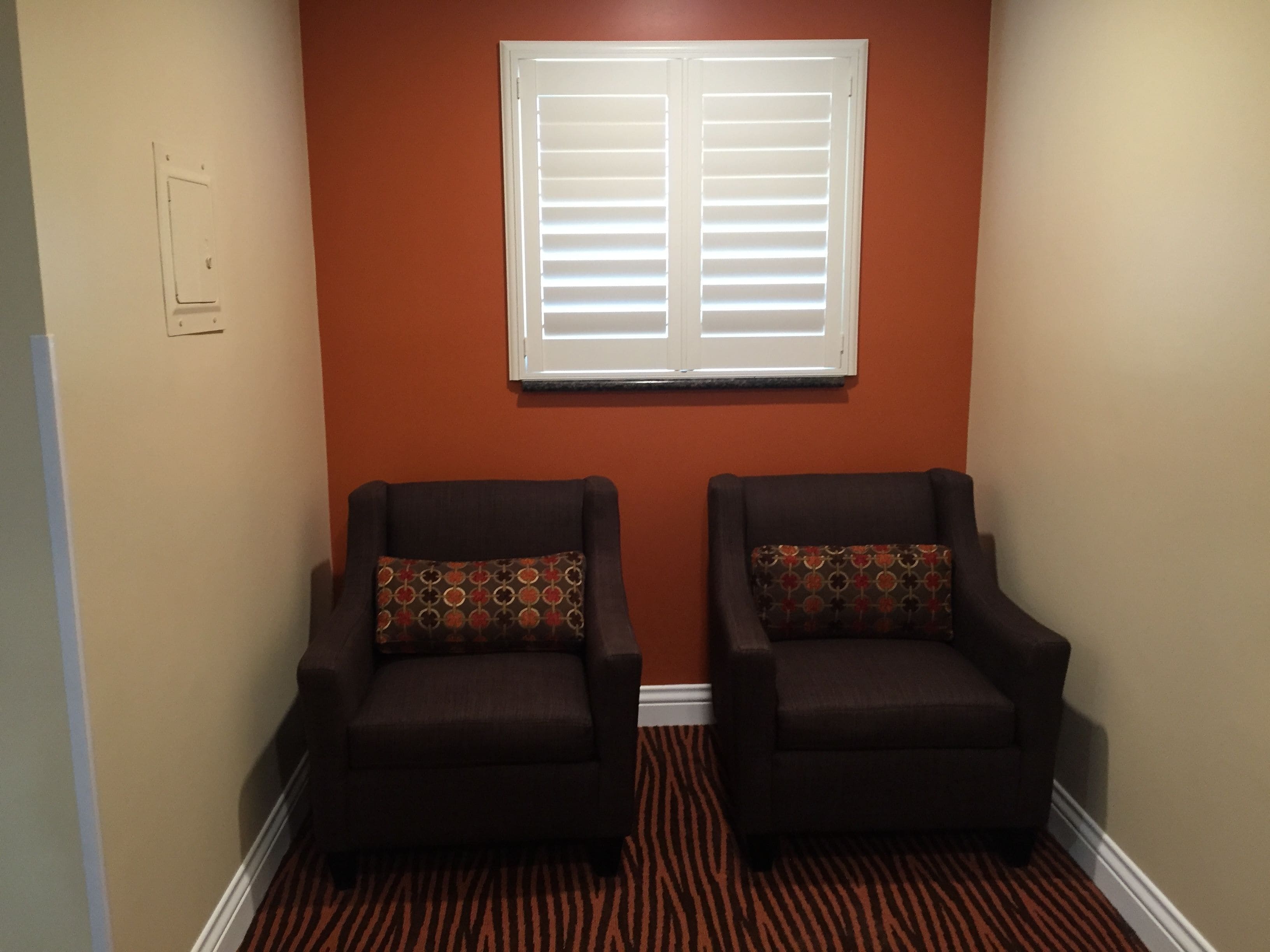 A hallway with two armchairs, a patterned rug, and a window with blinds.