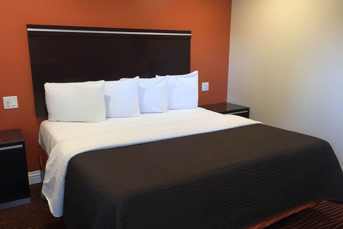 Una habitación de hotel con una cama grande, ropa de cama blanca, un cabecero oscuro y una mesita de noche pequeña.