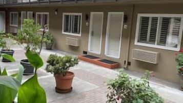 Un immeuble à plusieurs étages doté de balcons, de plantes en pot et d’une cour dallée.