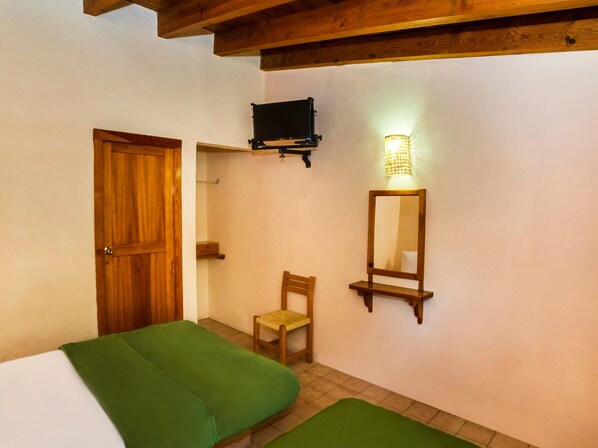 Une chambre avec deux lits, une porte en bois, une chaise, un téléviseur fixé au mur et un luminaire fixé au mur.