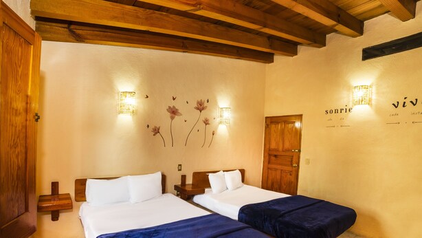 A hotel room with two beds, wooden beams on the ceiling, a wall with floral wall art, and a door with a sign. - Posada Valle de Bravo (Valle de Bravo)