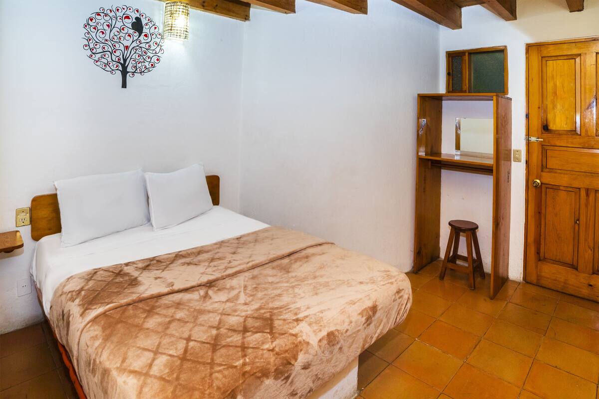 A bedroom with a bed, a wooden wardrobe, a small stool, and a wall decoration.