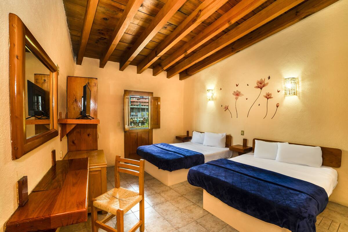 A hotel room with two beds, wooden furniture, a desk, a chair, a TV, and a window with a view of a building.