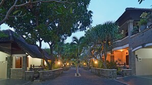 A paved pathway flanked by buildings with traditional architecture, surrounded by lush greenery. - Taman Ayu 212 (Denpasar)