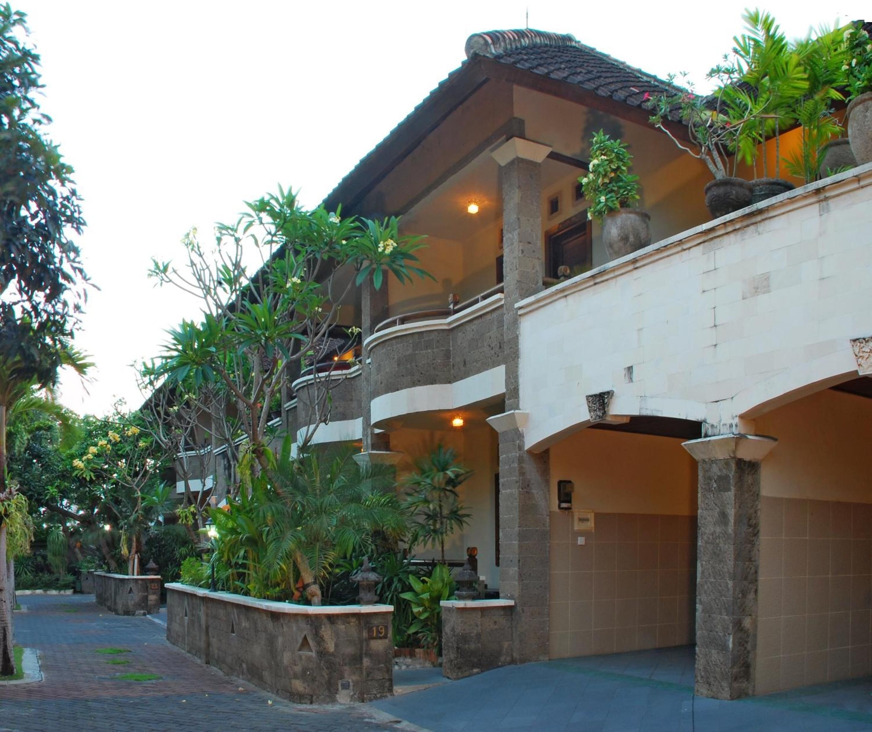 A multi-story building with a balcony, surrounded by lush greenery and potted plants.