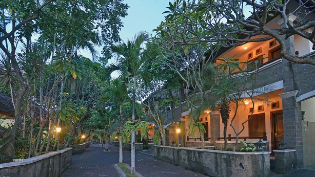 A pathway lined with trees and a building with a balcony. - Taman Ayu 212 (Denpasar)