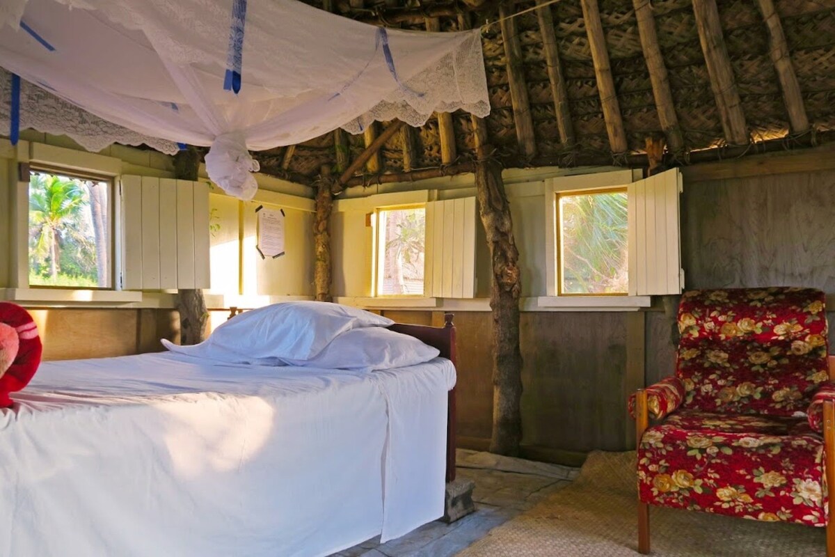 A room with a bed, a chair, and windows with shutters.