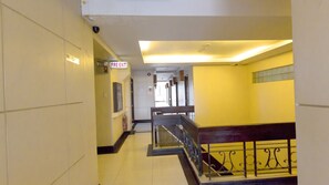 A corridor with a fire exit sign, a bench, and a staircase with a metal railing.