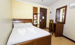 A hotel room with a wooden bed, a desk, and a chair. There is a telephone on the desk and a mirror on the wall.